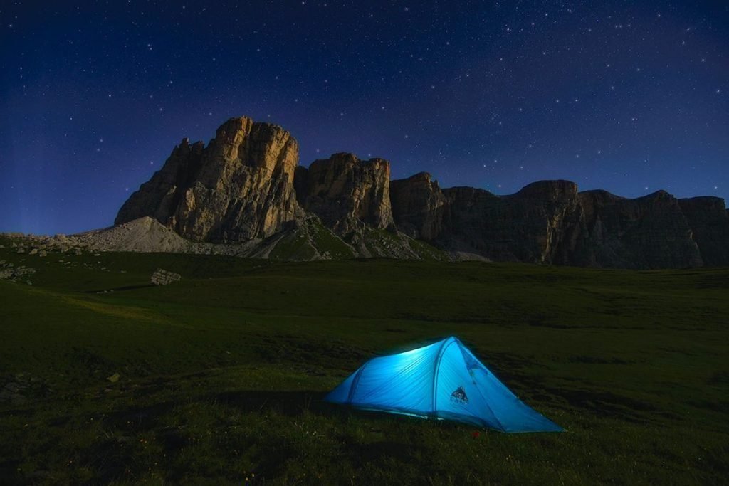 tent illuminated in dark by mountains
